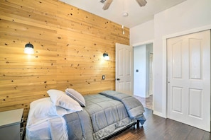 Een slaapkamer met een houten wand, een bed met een grijze dekbedovertrek, en twee wandlampen.