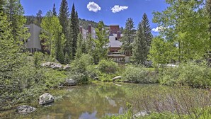 A lodge with a pond, surrounded by trees and mountains.