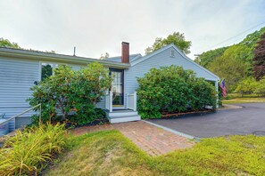 A single-story house with a front porch, a chimney, and a small front yard with grass and shrubs.