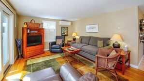 Ein Wohnzimmer mit einer Couch, Sesseln, einem Couchtisch, einem Fernseher auf einem Holzständer und einem gemusterten Teppich.