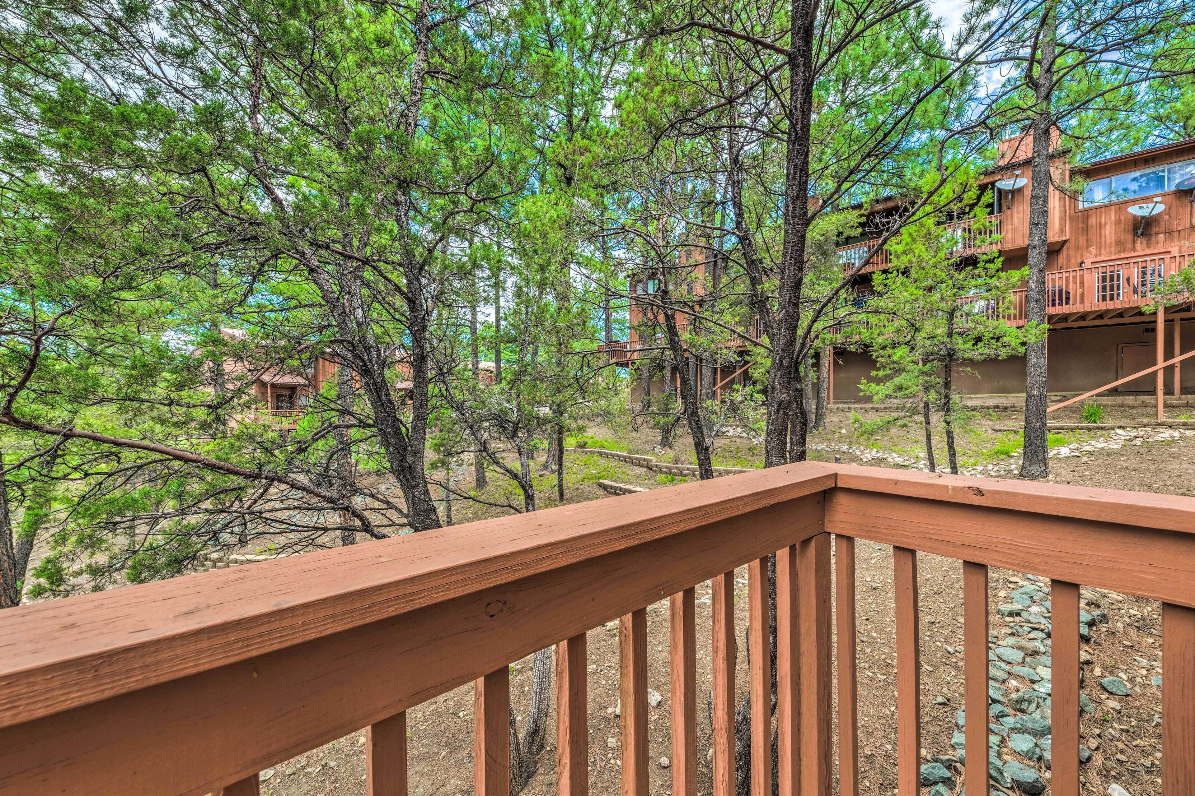 A wooden deck with a view of a forested area and a building with multiple levels and balconies.