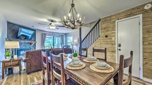 A dining area with a wooden table set for four, surrounded by chairs, a chandelier, and a television mounted on the wall. - Rustic Ruidoso Retreat Near Shops & Mountains! (Ruidoso)