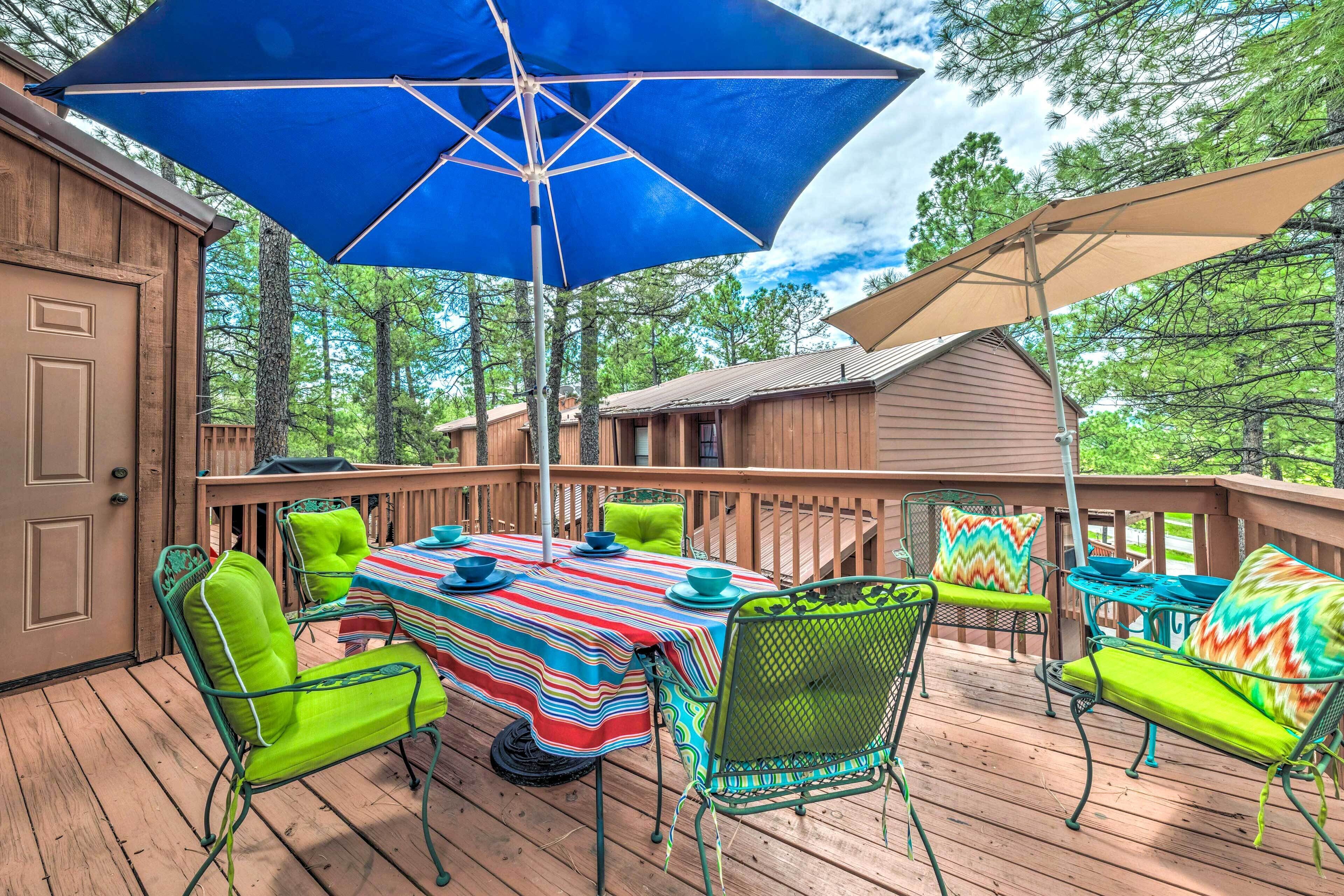 Une terrasse en bois avec une table et des chaises, un parasol bleu et un auvent de couleur beige.
