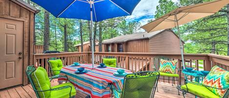 Une terrasse en bois avec une table et des chaises, un parasol bleu et un auvent de couleur beige.