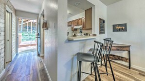 A modern kitchen with wooden cabinets, a bar area with stools, and a view of the backyard through an open door. - Rustic Ruidoso Retreat Near Shops & Mountains! (Ruidoso)