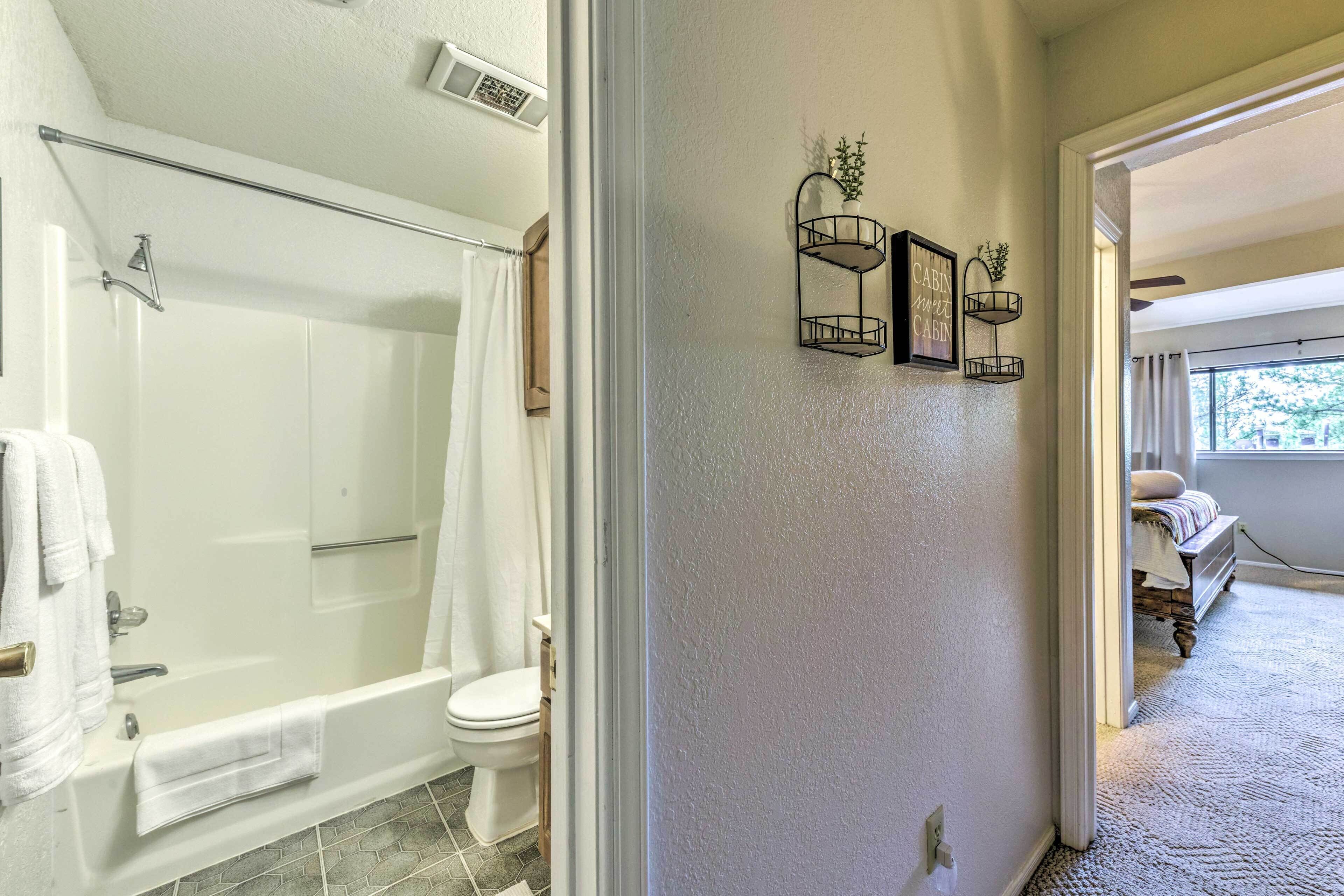 A bathroom with a bathtub, toilet, and shower curtain. There are wall-mounted shelves with decorative items.