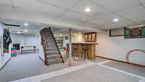 Amplia habitación con escalera, zona de bar con taburetes y dardos en la pared.