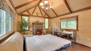 Una camera da letto accogliente in legno con un letto, un camino, un tavolo da pranzo con sedie e un'ampia finestra.