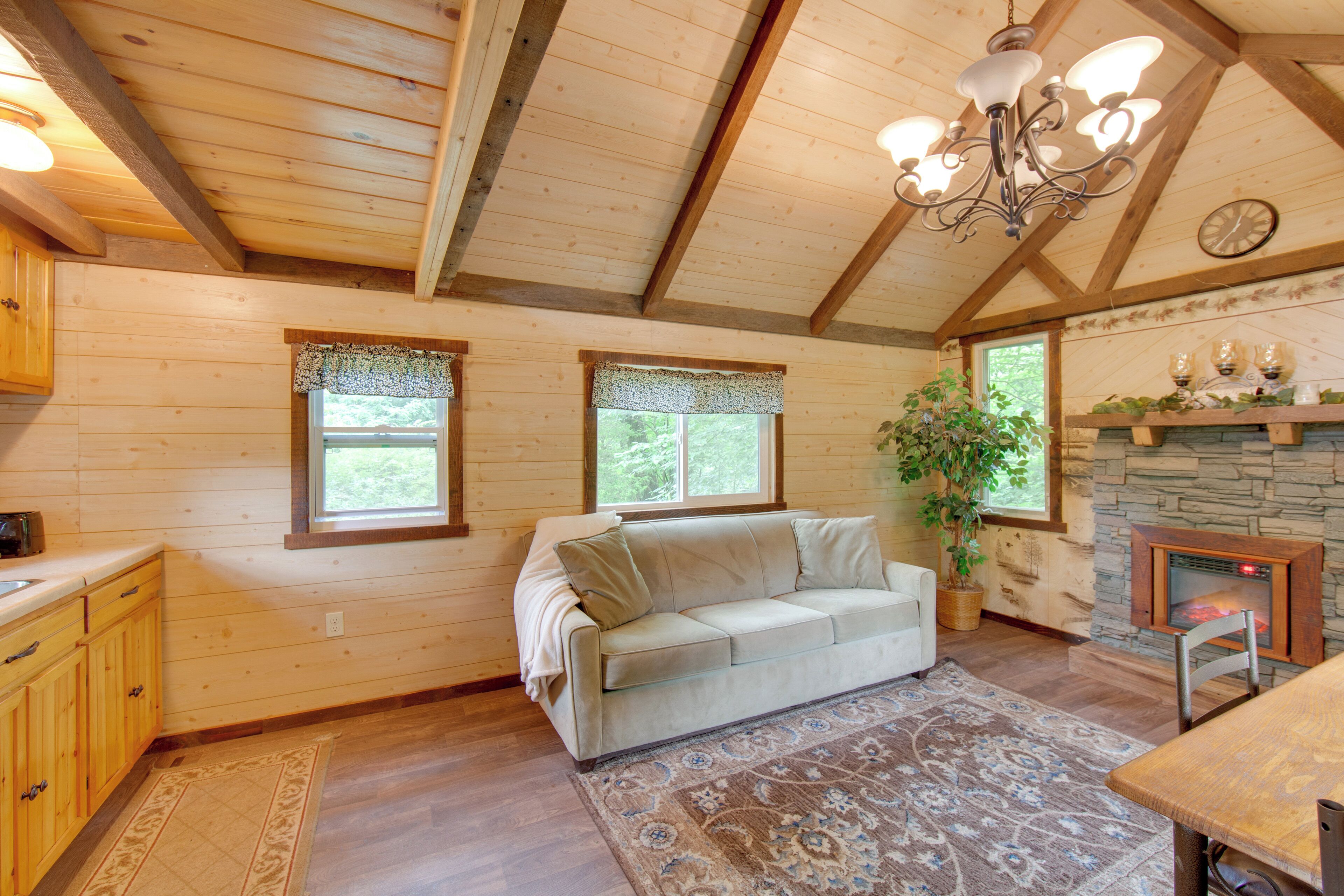 A cozy cabin interior with a wooden ceiling, a fireplace, a sofa, and a dining area.
