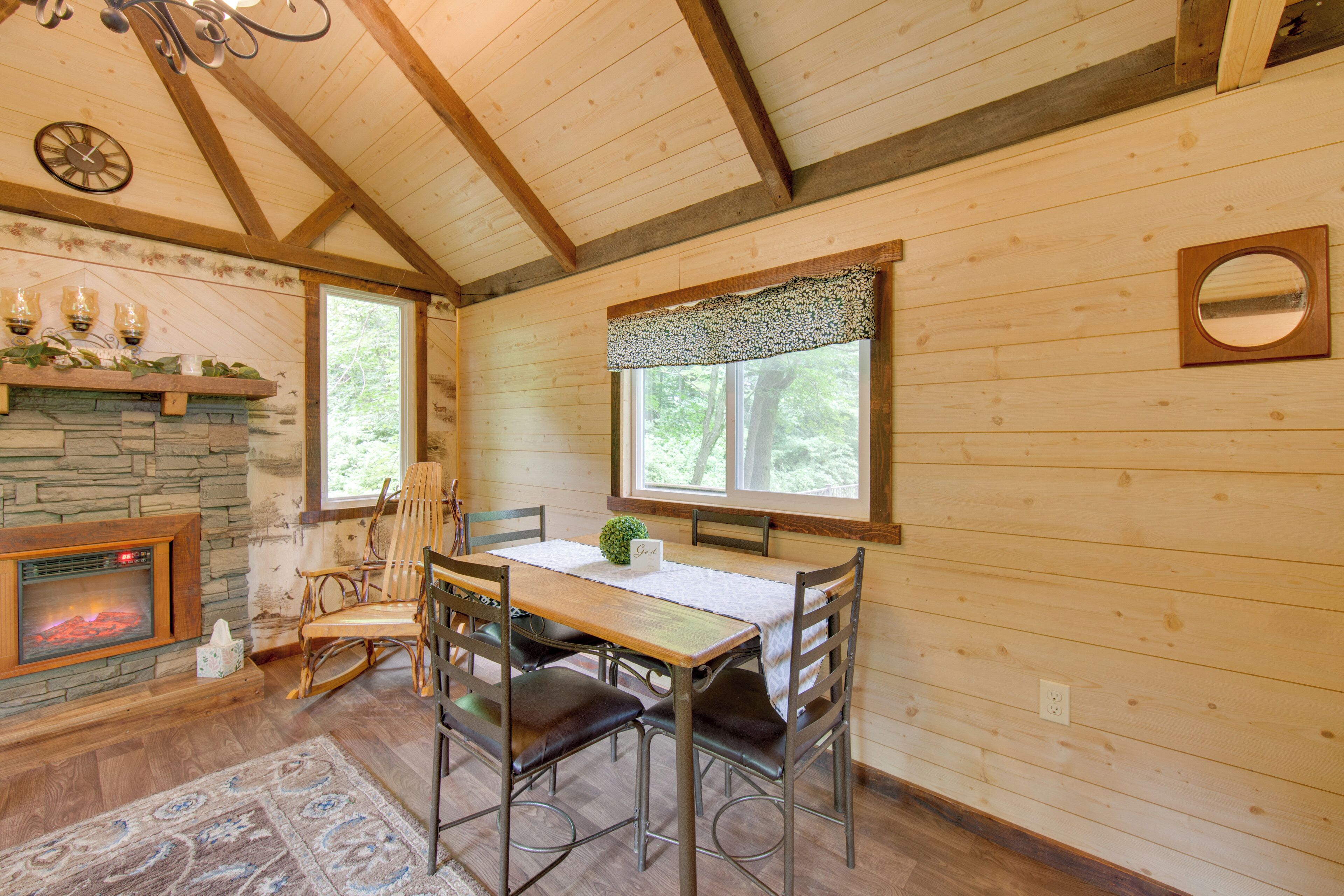 A cozy cabin interior with a stone fireplace, wooden dining table, and chairs.