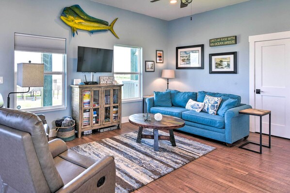 A living room with a blue sofa, a leather chair, a wooden coffee table, a fish decoration, a TV, and a bookshelf.