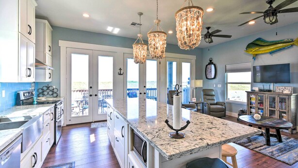 A spacious kitchen with granite countertops, white cabinets, and a large island. There are pendant lights, ceiling fans, and a view to the outside. - Waterfront Sargent House w/ Sparkling Pool! (Bay City)