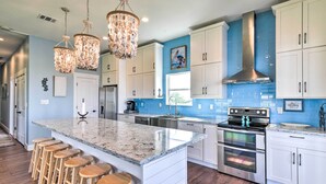 A modern kitchen with a large island, stainless steel appliances, and a blue accent wall. - Waterfront Sargent House w/ Sparkling Pool! (Bay City)