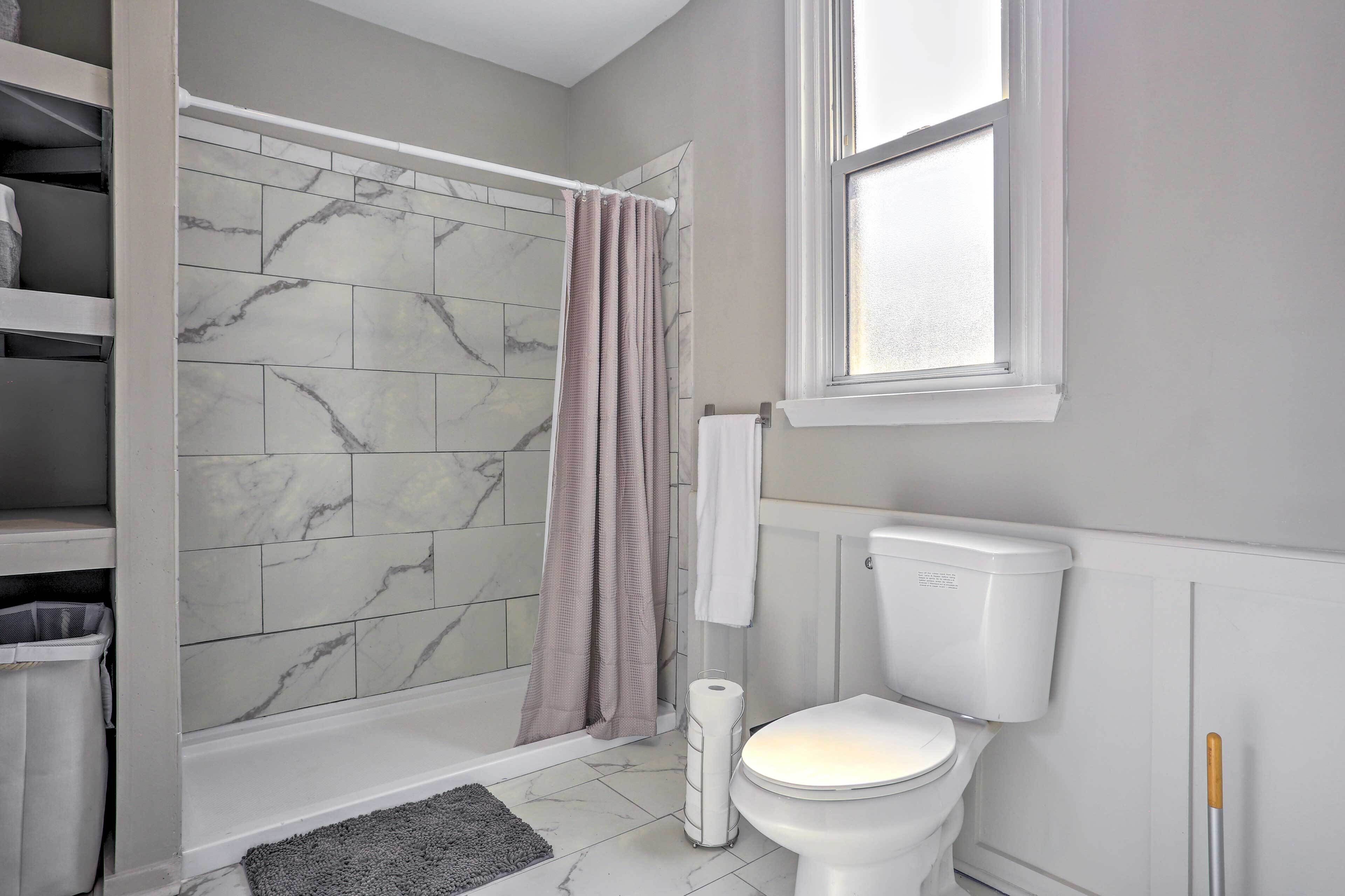 A bathroom with a shower, toilet, and marble tiles.