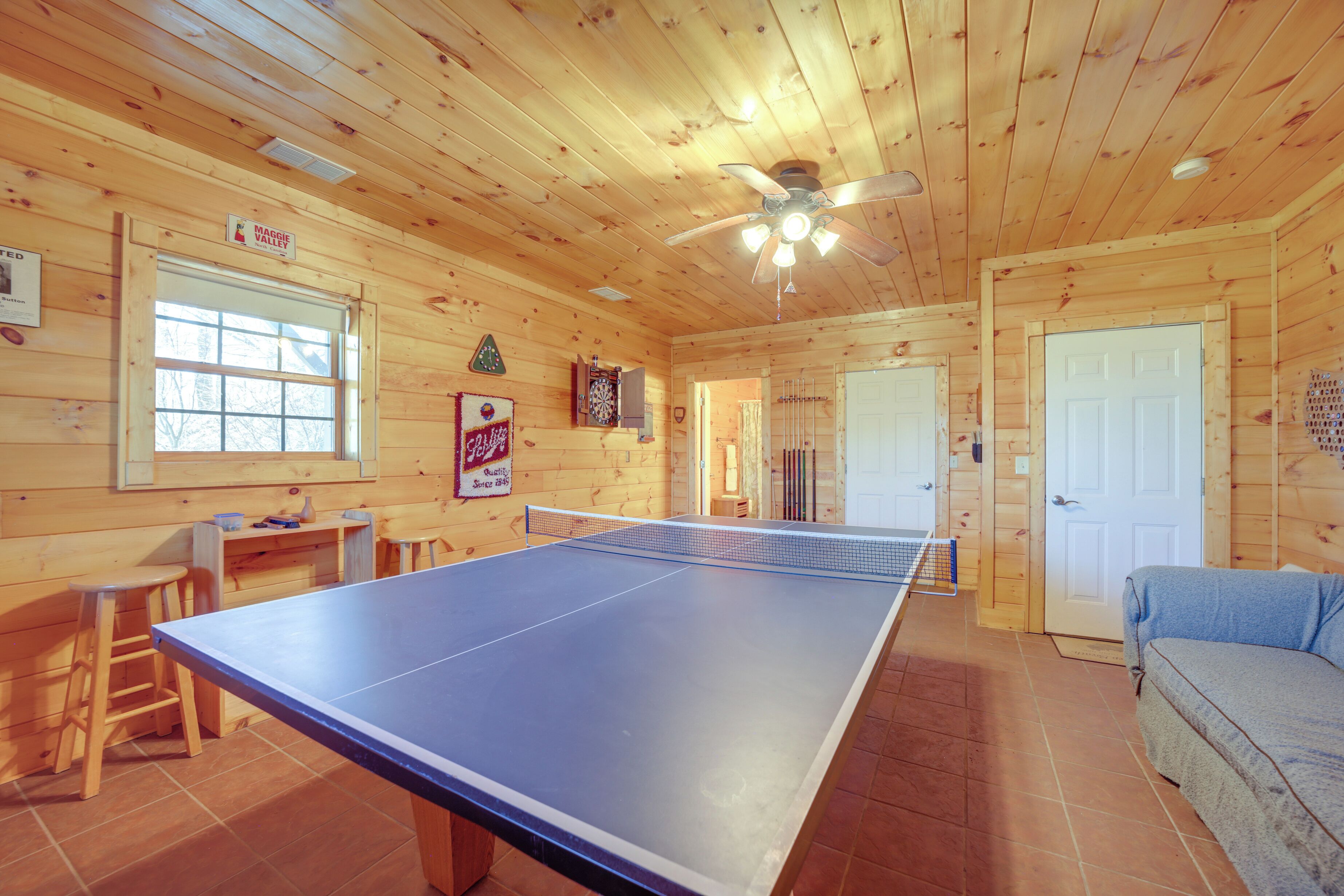 Une table de ping-pong se trouve dans une pièce en bois, dotée d’un ventilateur au plafond, de murs en bois et d’une porte.
