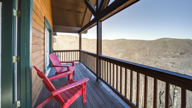 Un porche de madera con dos sillas Adirondack rojas y vistas a un paisaje montañoso.