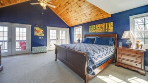Un dormitorio con techo de madera, una cama grande, una mesita de noche, un banco y un cuadro en la pared.