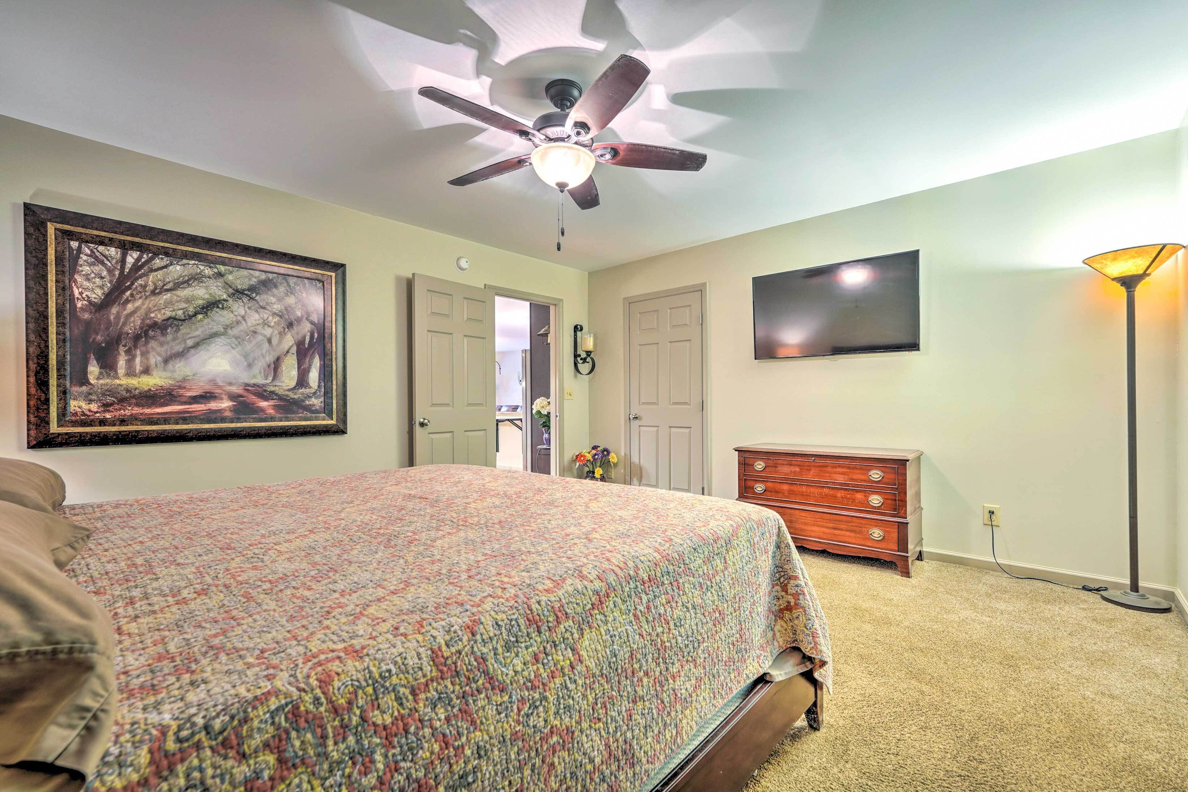 A bedroom with a bed, a ceiling fan, a dresser, a lamp, and a painting on the wall.