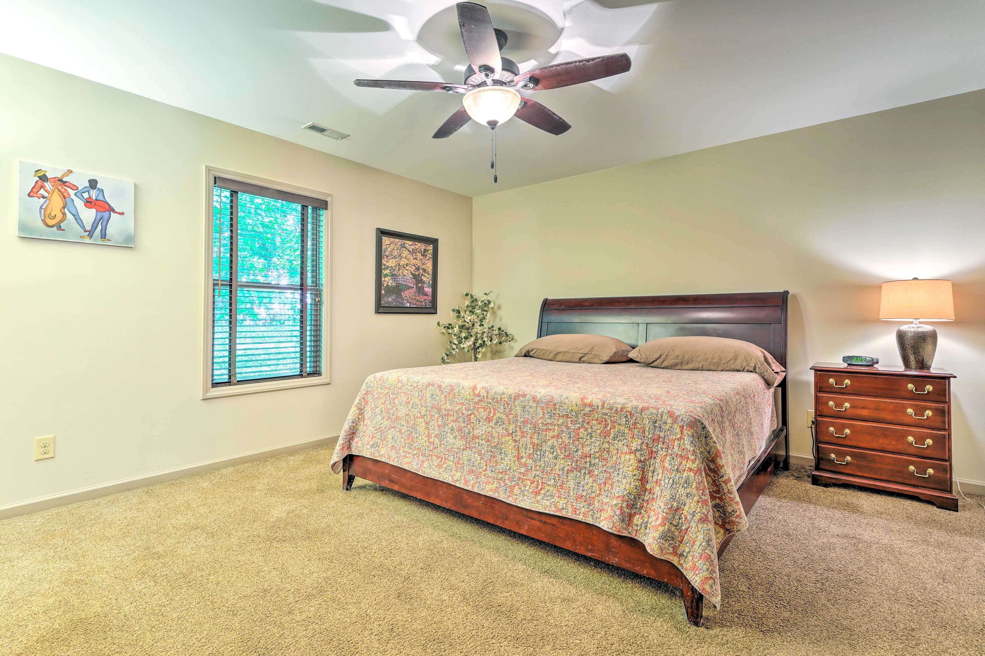 A bedroom with a bed, a ceiling fan, a dresser, and a window with blinds.