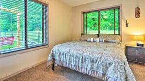 A bedroom with a large bed, a nightstand, a lamp, and a window with blinds.