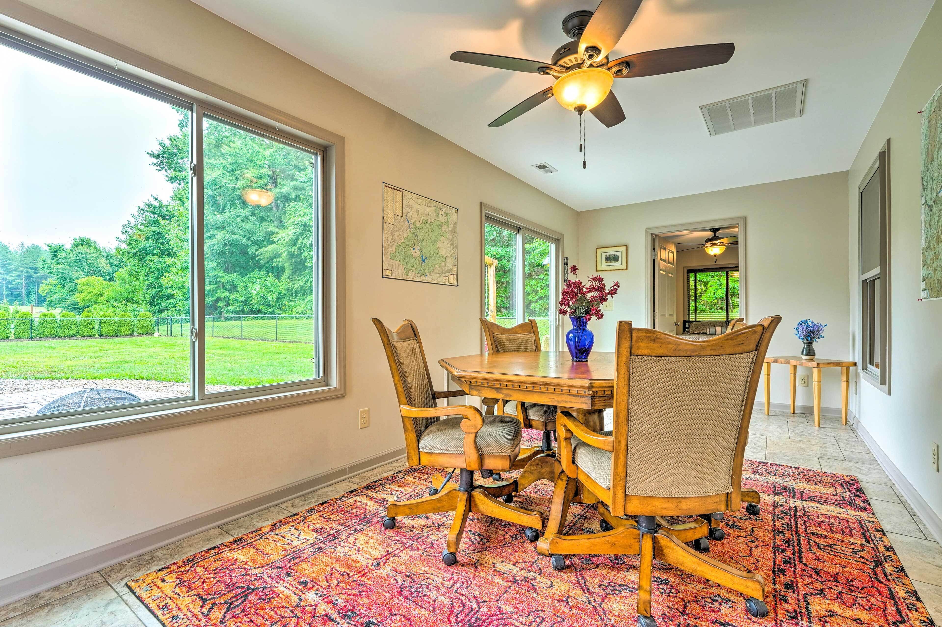 A dining area with a large window, a ceiling fan, and a patterned rug.