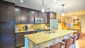 A modern kitchen with dark wood cabinets, granite countertops, stainless steel appliances, and a bar area with stools.