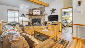 A cozy living room with a stone fireplace, wooden furniture, and a television.