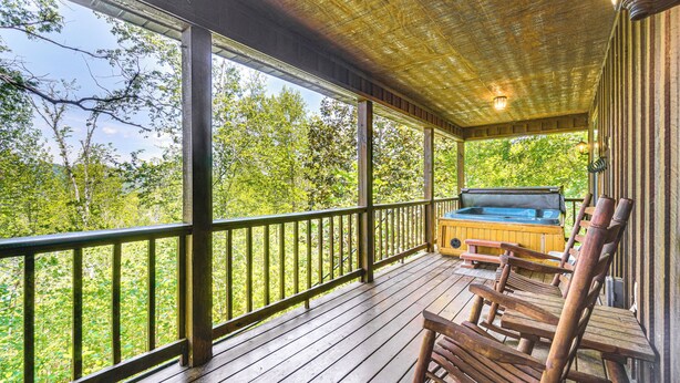 A wooden deck with a hot tub and seating area, overlooking a forested area.