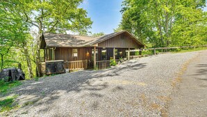 A rustic cabin with a gravel driveway, surrounded by trees.