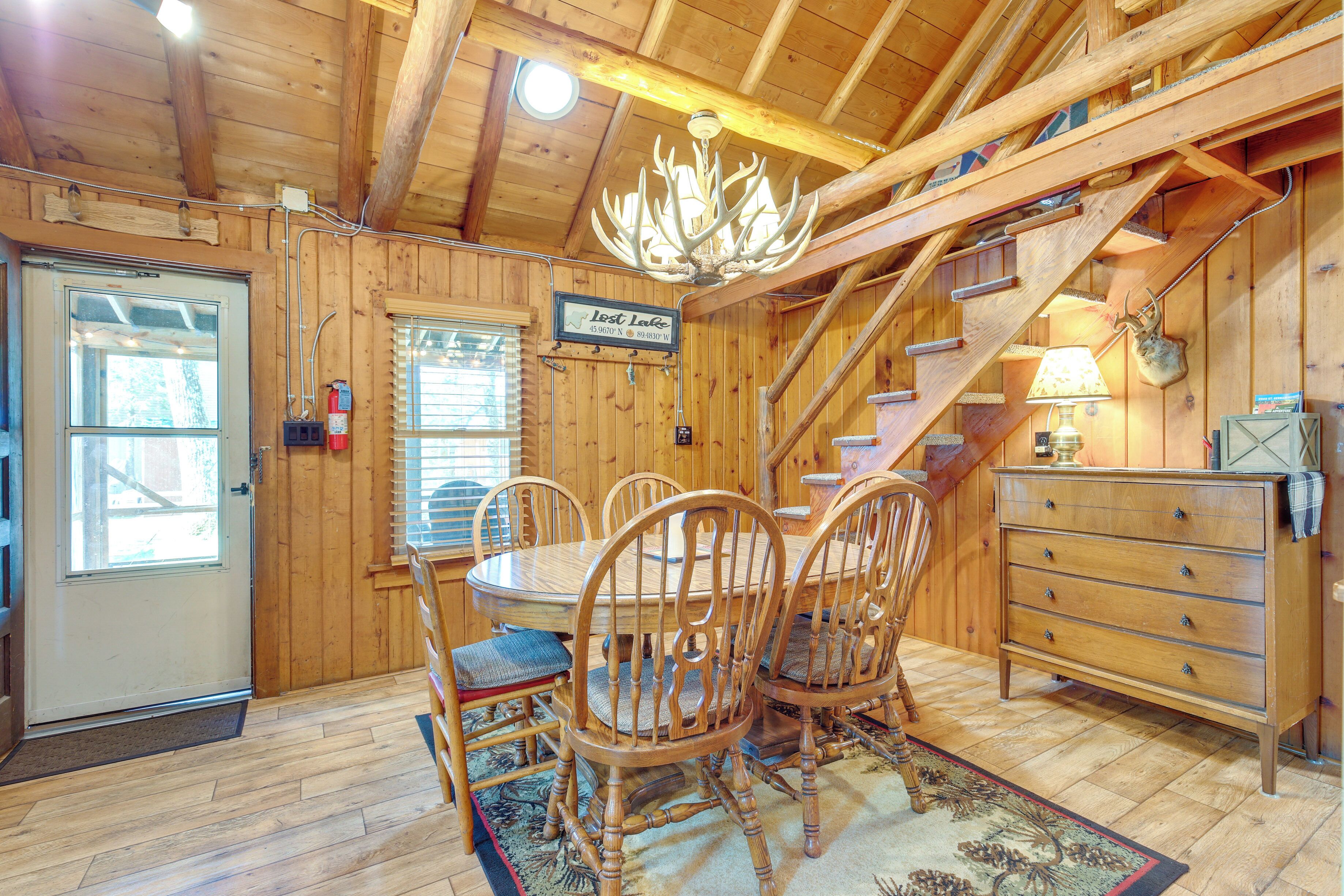 A wooden interior with a dining table, chairs, a chandelier, a staircase, and a sign reading "Lost Lake".