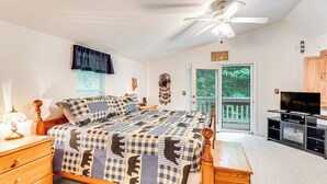A bedroom with a checkered bedspread, a wooden dresser, a nightstand, a ceiling fan, a television, and a sliding glass door leading to a balcony. - Secluded Cabin w/ Porch - 7 Miles to Lake Chatuge! (Hayesville)
