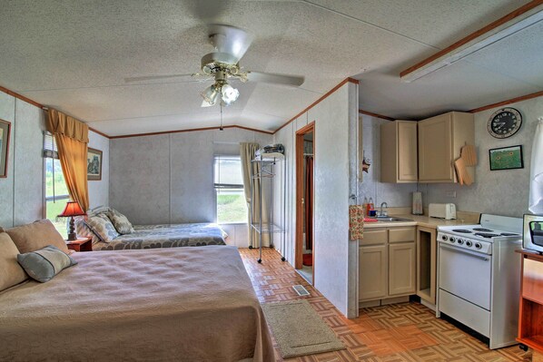 Un dormitorio con dos camas, ventilador de techo y kitchenette con estufa y alacenas.