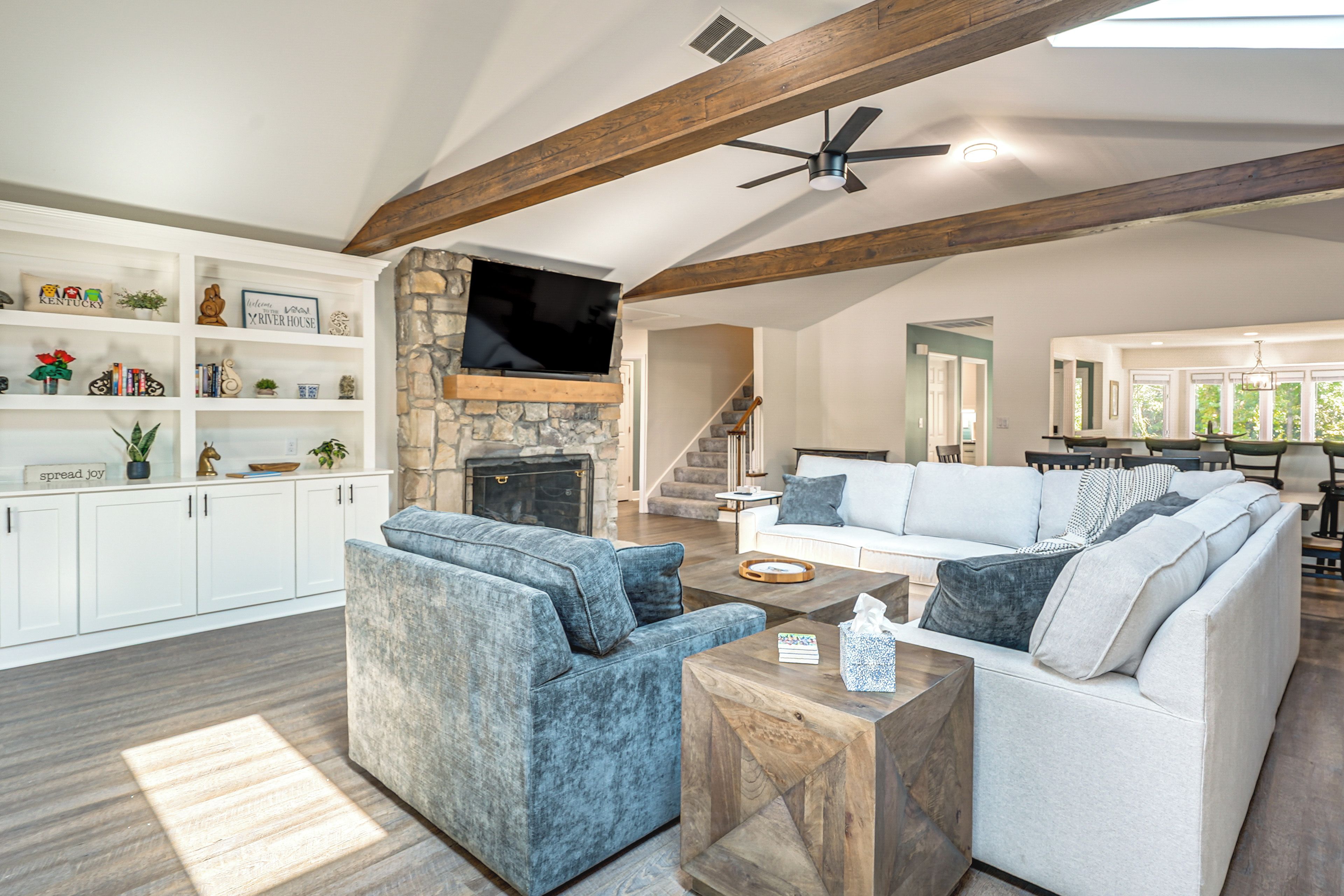 A spacious living room with a fireplace, a television mounted on a stone wall, and a dining area with a view of the outdoors.