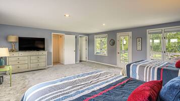 A bedroom with two beds, a dresser, a television, and a window with a view of greenery.