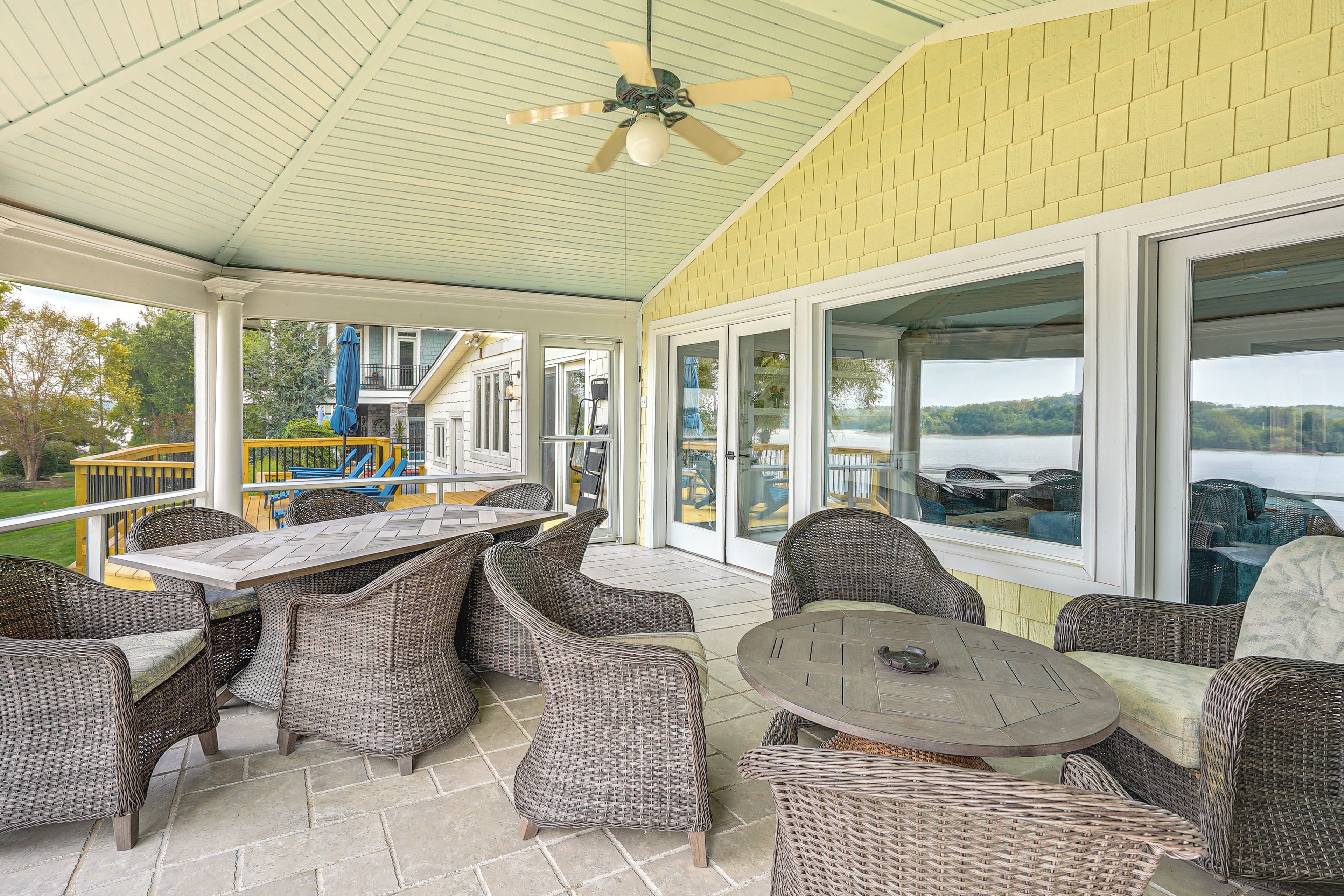 A covered patio with wicker furniture, large windows, and a view of a lake.