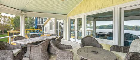 A covered patio with wicker furniture, large windows, and a view of a lake.