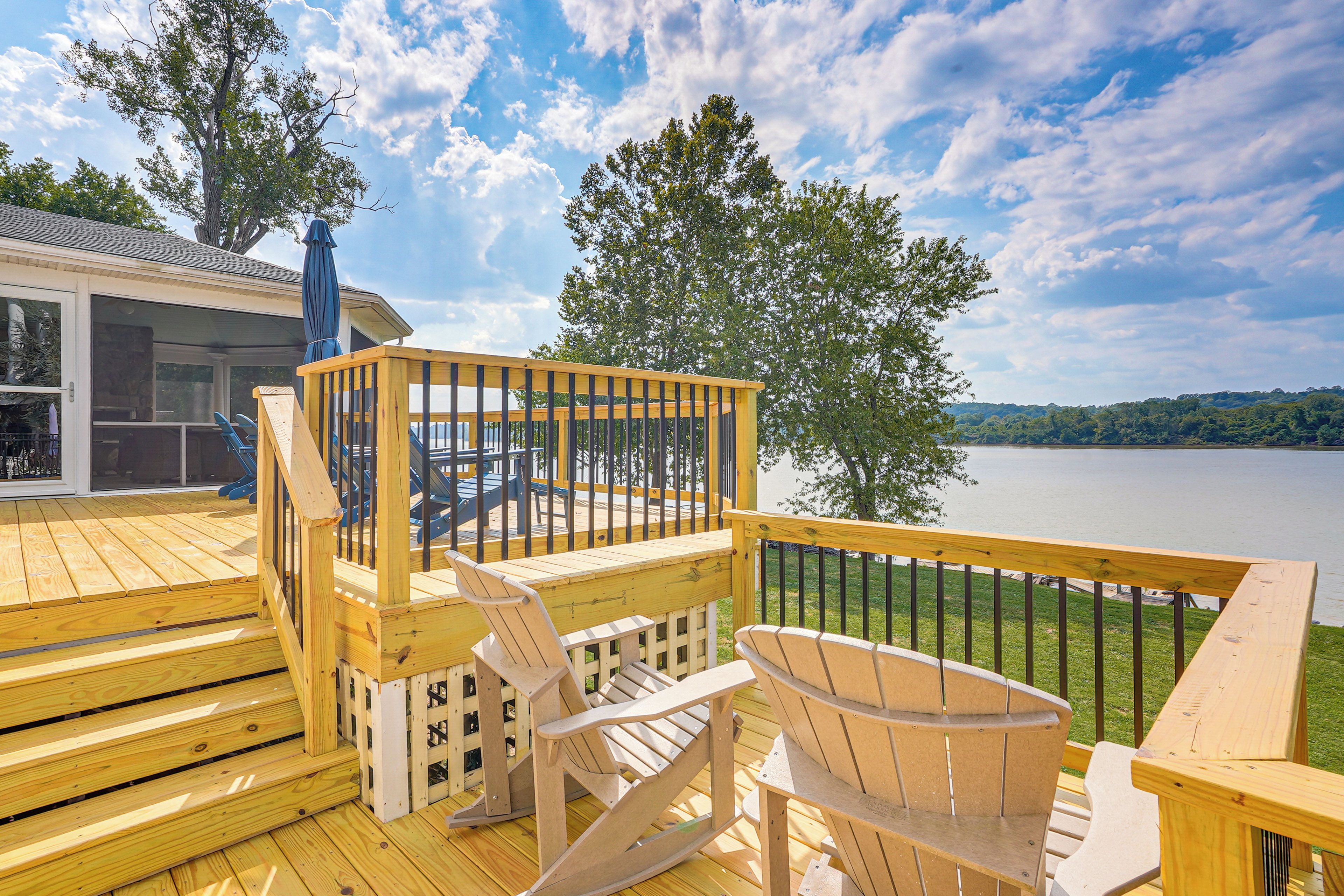 Terraza de madera con vistas a un lago, con una silla y una mesa de madera.