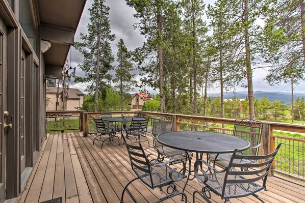 A wooden deck with outdoor furniture, overlooking a scenic landscape with trees and distant mountains.