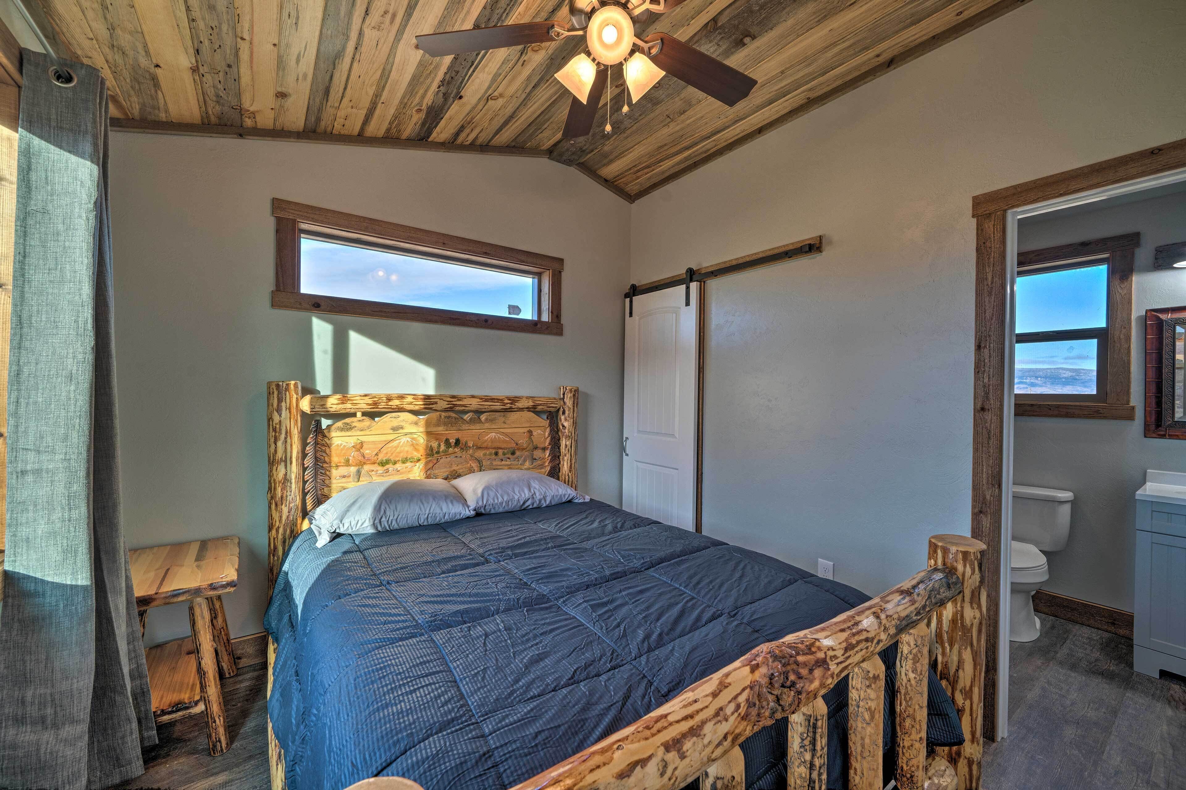 A bedroom with a wooden headboard, a bed with a blue quilt, a small wooden nightstand, a ceiling fan, and a window.