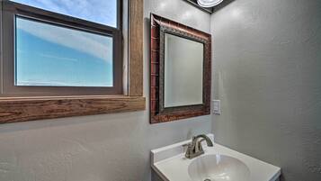A bathroom with a window, a sink, and a mirror with an ornate frame.