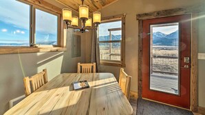 A wooden dining table with a book, a chandelier, and a view of mountains through a door. - Romantic Gem w/ Mtn Views! Day Trip to Yellowstone (Livingston)