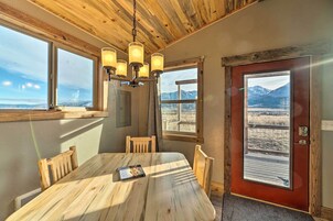Una mesa de madera para comer con un libro, un candelabro y vistas de montañas a través de una puerta.