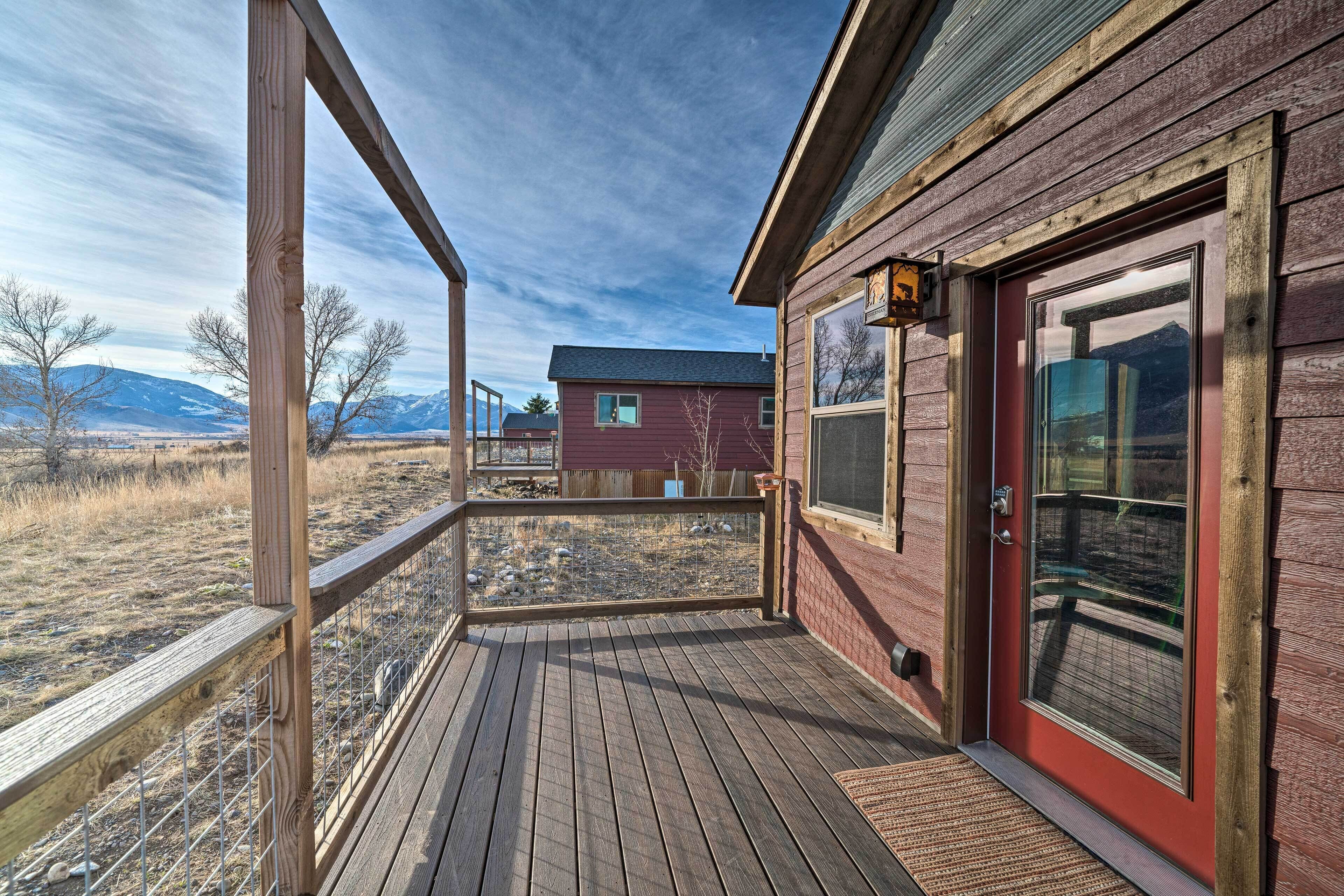 A wooden deck with a metal railing, a red door, and a window.