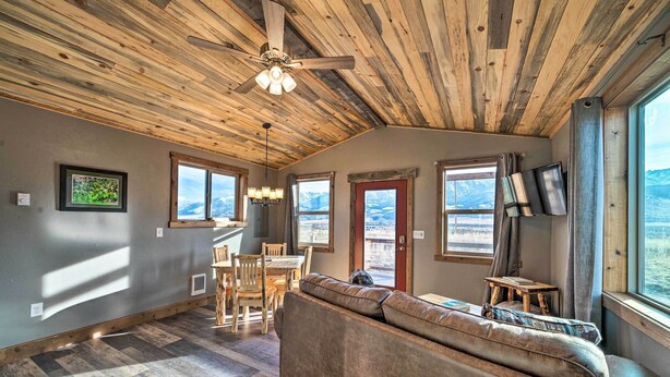 A spacious living area with a wooden ceiling, a sofa, a dining table, and a TV mounted on the wall. - Romantic Gem w/ Mtn Views! Day Trip to Yellowstone (Livingston)