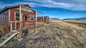A rustic cabin with a wooden deck and a metal roof, surrounded by a dry, grassy landscape. - Romantic Gem w/ Mtn Views! Day Trip to Yellowstone (Livingston)