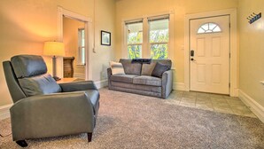Un salón con un sillón de cuero gris, un sofá gris con almohadas, una lámpara y una puerta con ventanal.