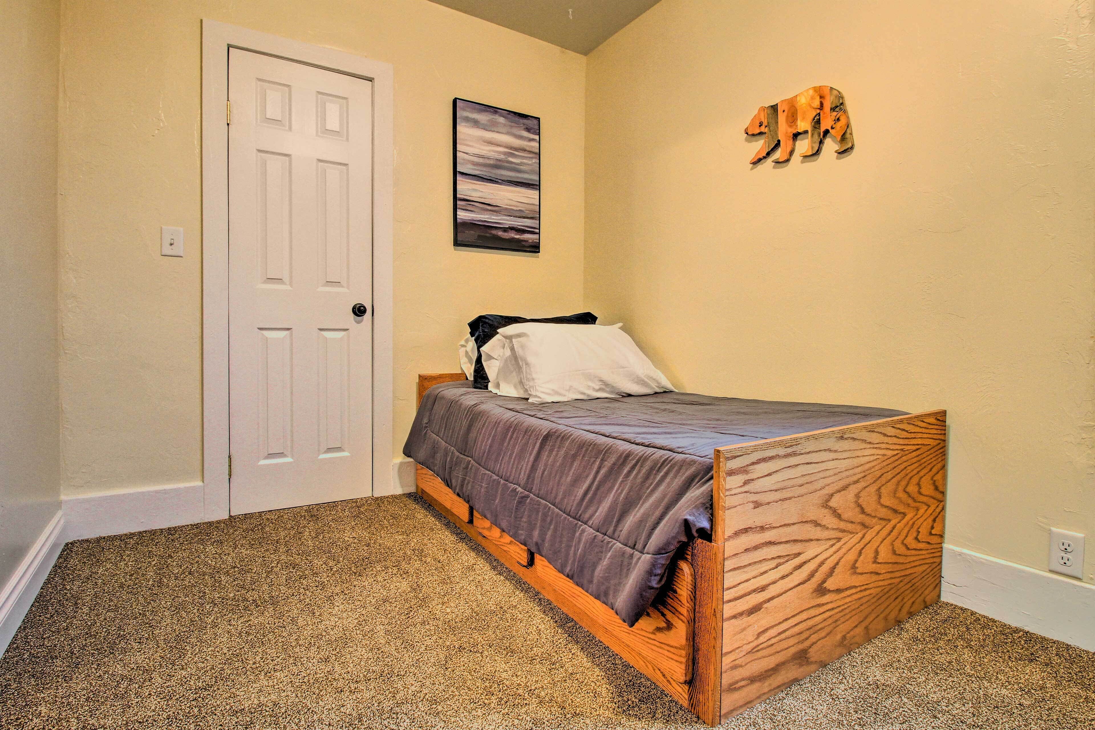 A bedroom with a wooden bed frame, a white door, a painting on the wall, and a wooden bear decoration.