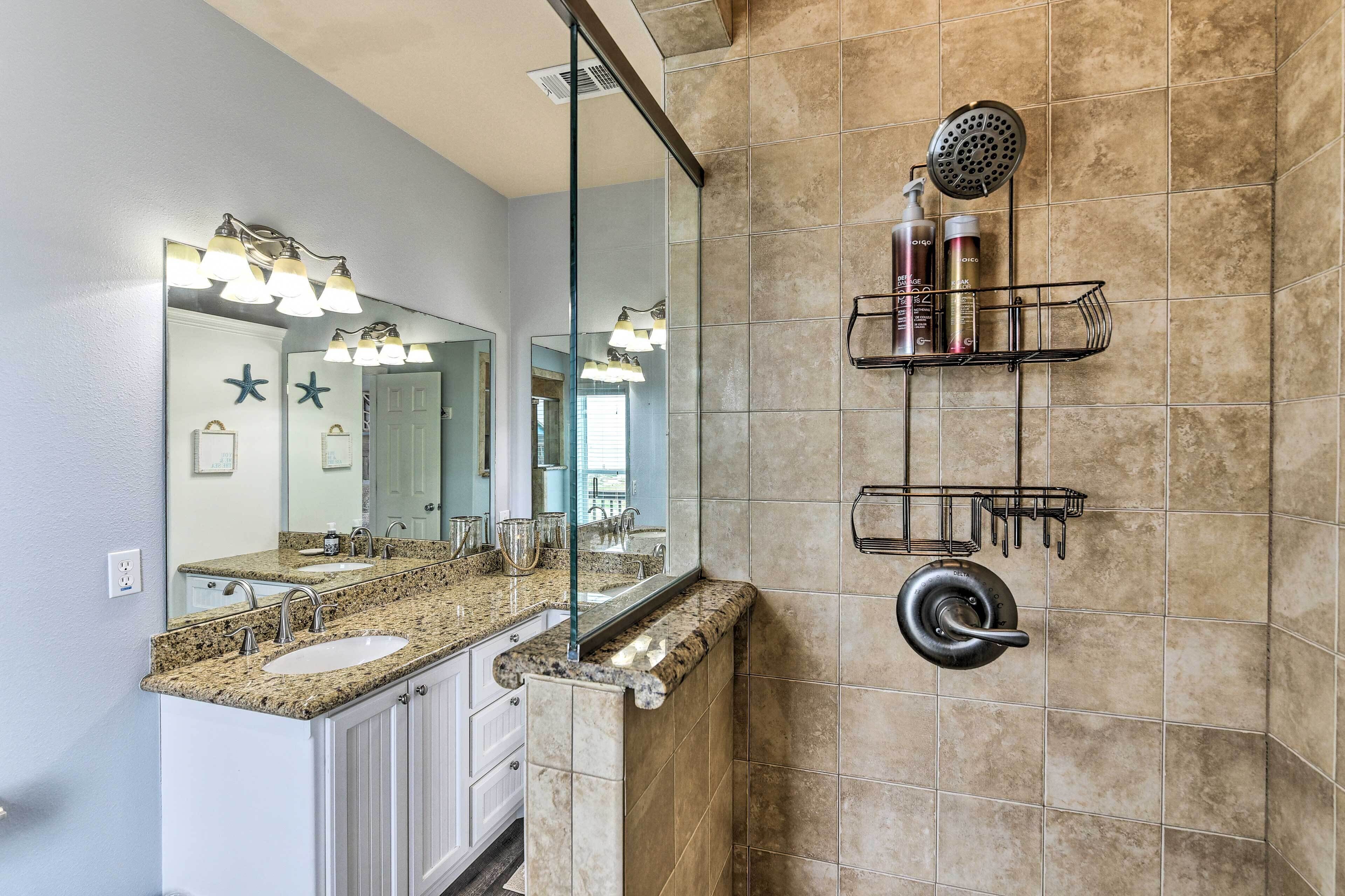 A bathroom with a granite countertop, a large mirror, a shower with a handheld showerhead, and a towel rack.