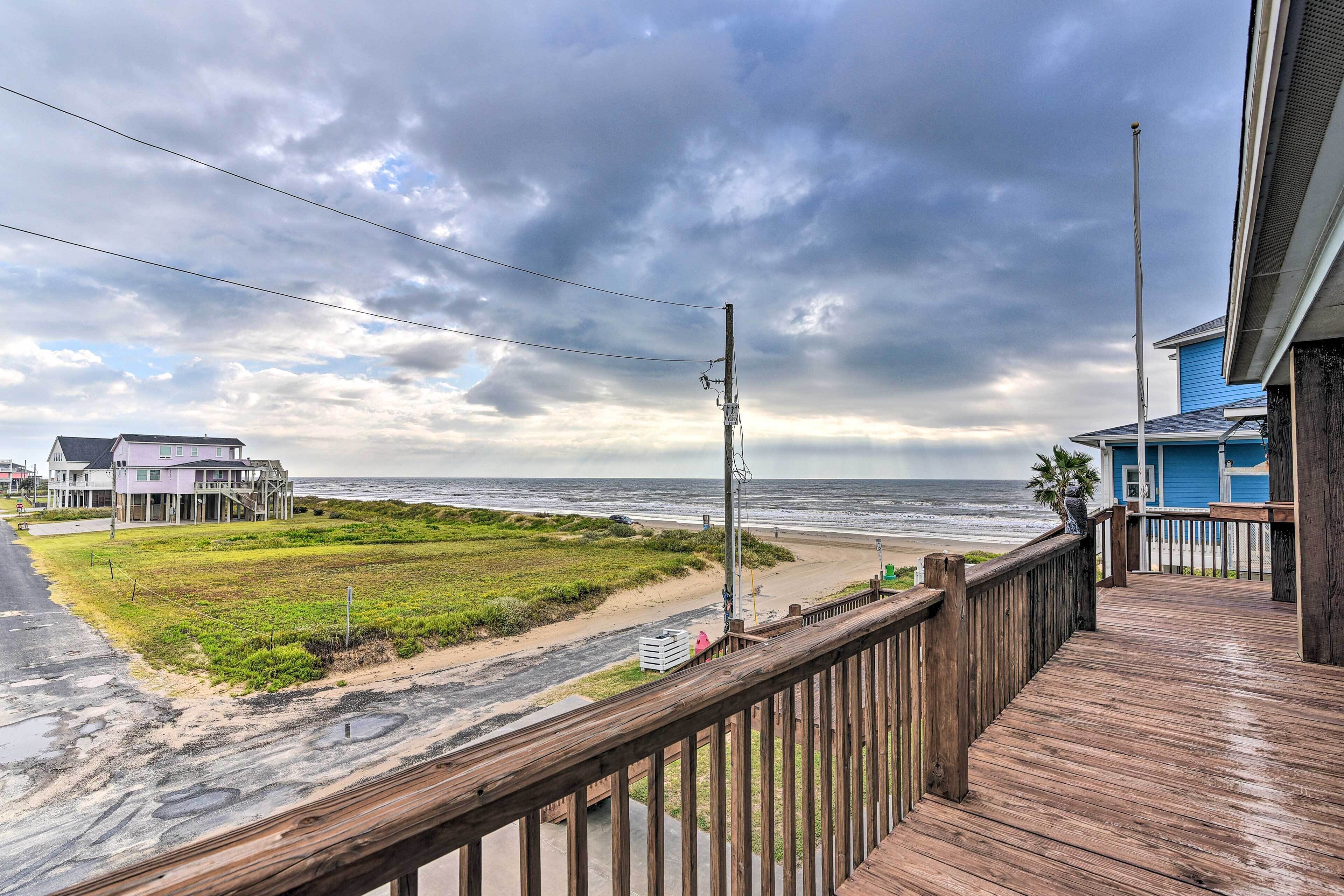 A wooden deck overlooking a beach with a view of the ocean and a house in the background.