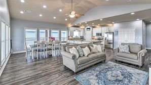 A spacious living room with a gray sofa, a blue rug, and a dining area with a table and chairs. - Group Getaway w/ Deck, Steps to Crystal Beach! (Port Bolivar)